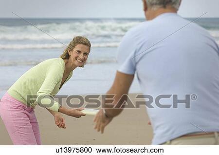 Stock Image - Couple playing frisbee on a beach. Fotosearch