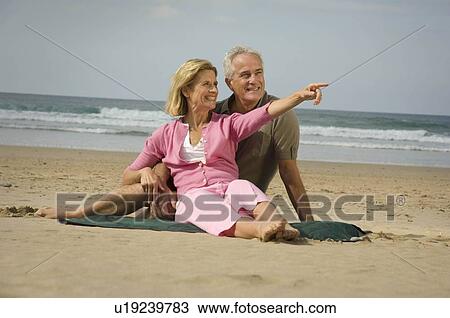 Stock Image - Couple sat on a beach. Fotosearch