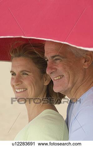 Couple sheltering under beach parasol View Large Photo Image Stock Image - Couple sheltering under beach parasol. Fotosearch