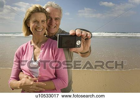 Stock Photo - Couple taking photograph on a beach. Fotosearch