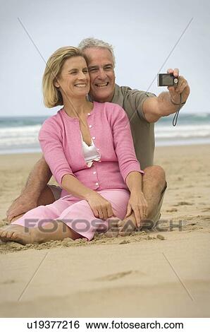 Couple taking photograph on a beach View Large Photo Image Stock Photograph - Couple taking photograph on a beach. Fotosearch