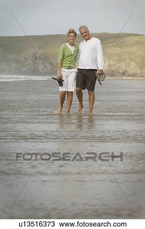 Stock Image - Couple walking arm in arm on a beach. Fotosearch