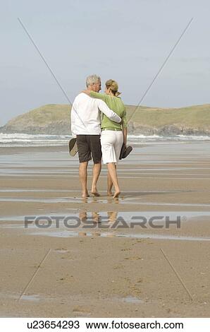 Couple walking arm in arm on a beach View Large Photo Image Stock Image - Couple walking arm in arm on a beach. Fotosearch