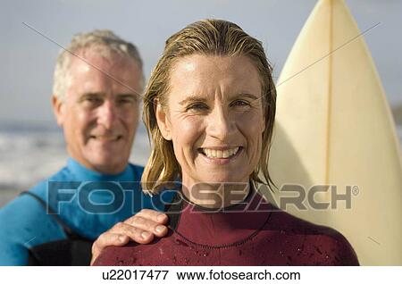 Couple wearing wetsuits on a beach View Large Photo Image Stock Photo - Couple wearing wetsuits on a beach. Fotosearch