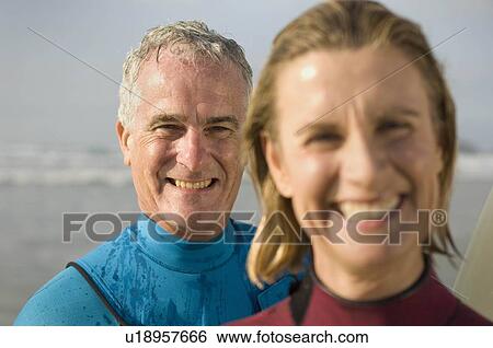 Stock Photograph - Couple wearing wetsuits on a beach. Fotosearch
