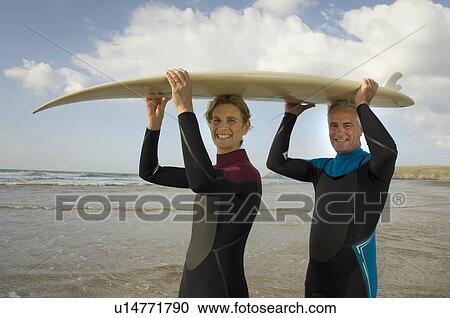 Couple with surfboard on a beach View Large Photo Image Stock Image - Couple with surfboard on a beach. Fotosearch