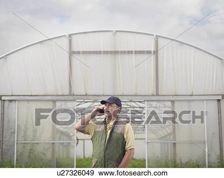 Stock Photo - Farmer On Mobile Outside Polytunnel. Fotosearch