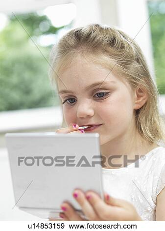 Stock Photo - Girl looking in mirror with lipstick. Fotosearch