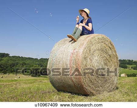 Stock Photo - Girl on bale of hay blowing bubbles. Fotosearch