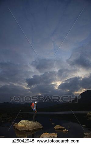 Stock Photography - Hiker standing on rocks in a lake.. Fotosearch