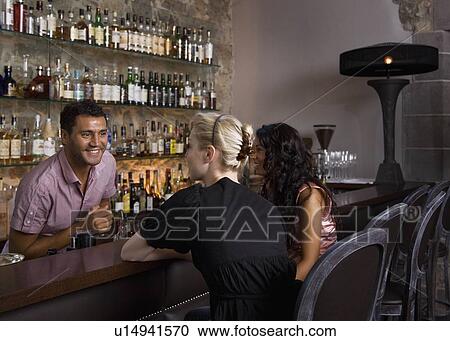 Stock Image - Male bartender taking customers orders. Fotosearch