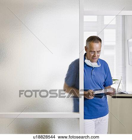 Picture - Male dentist looking over paperwork. Fotosearch
