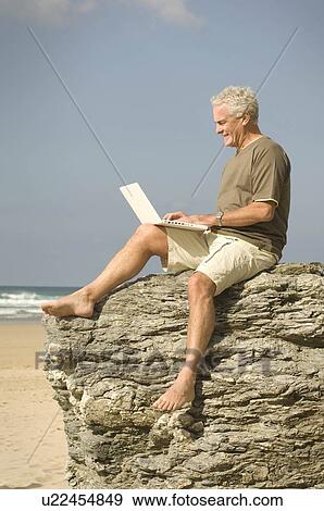 Stock Photo - Male on a beach using his computer. Fotosearch