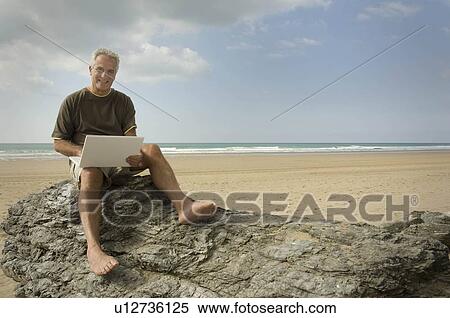 Stock Photography - Male on a beach using his computer. Fotosearch