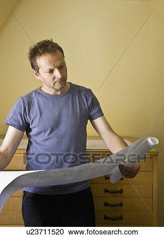 Stock Image - Man looking over blue prints. Fotosearch