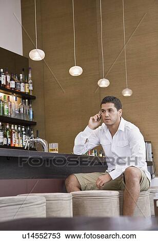 Stock Image - Man sitting at bar on cell phone. Fotosearch