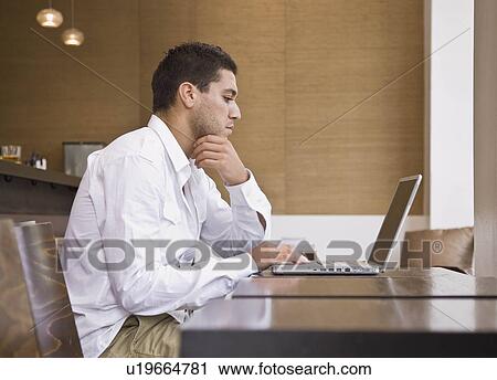 Stock Image - Man sitting at bar on laptop. Fotosearch