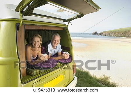 Stock Image - Mature couple lying in camper van. Fotosearch