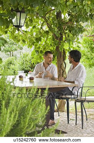 Men relaxing at table in a garden View Large Photo Image Stock Image - Men relaxing at table in a garden. Fotosearch