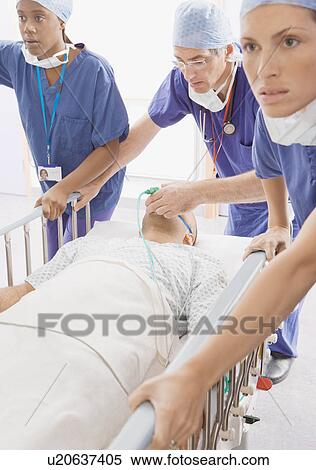 Stock Photography - Three doctors pushing a patient in bed. Fotosearch