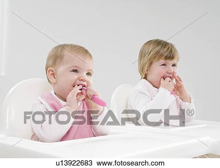 Stock Image - Two baby sisters in high chairs.. Fotosearch