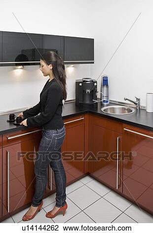 Stock Image - Woman making coffee in office kitchen. Fotosearch