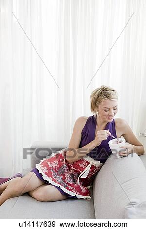 Stock Photo - Woman on sofa eating ice cream. Fotosearch