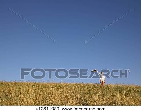 Stock Photo - Woman waving hat in field.. Fotosearch