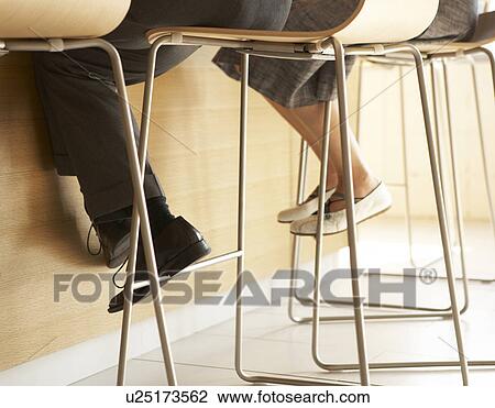 Stock Image - Low Section of Woman and Man Sitting on Stools. Fotosearch