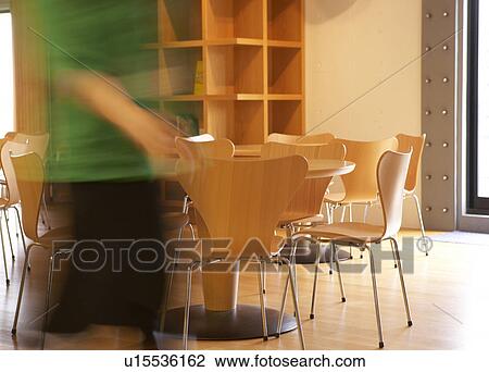 Stock Image - Woman Walking Near Tables and Chairs. Fotosearch