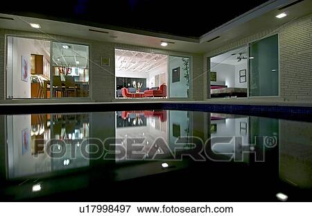 Stock Photo - Night view in towards living room of home across pool. Fotosearch