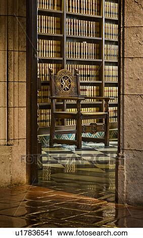 Stock Image - View through doorway to wood carved chair in front of bookcase. Fotosearch