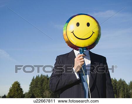Businessman holding smiley face balloon over face View Large Photo Image Stock Image - Businessman holding smiley face balloon over face. Fotosearch