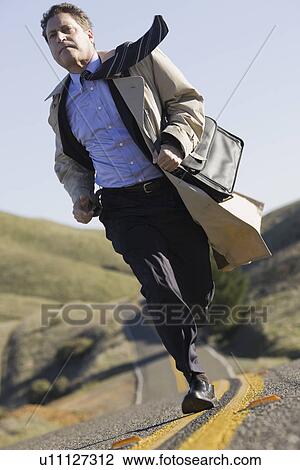 Stock Image - Businessman running on remote road. Fotosearch