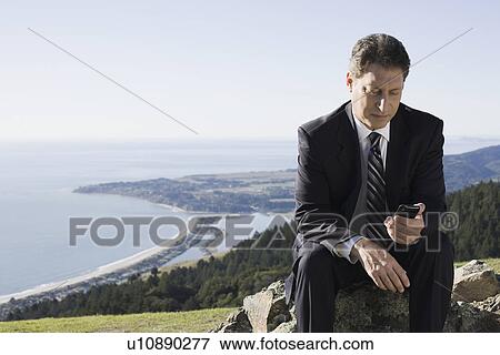 Businessman text messaging on remote hill View Large Photo Image Stock Photo - Businessman text messaging on remote hill. Fotosearch