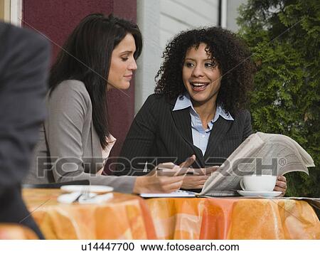 Businesswomen looking at stock pages at outdoor cafe View Large Photo Image Stock Image - Businesswomen looking at stock pages at outdoor cafe. Fotosearch