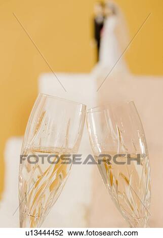 Stock Image - Close up of toasting champagne glasses and wedding cake. Fotosearch