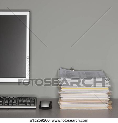 Stock Image - Computer and stack of paperwork. Fotosearch