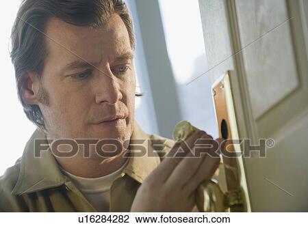 Stock Image - Locksmith repairing door lock. Fotosearch