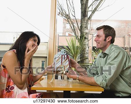 Stock Image - Man giving woman gift in restaurant. Fotosearch