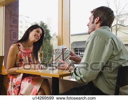 Stock Photo - Man giving woman gift in restaurant. Fotosearch