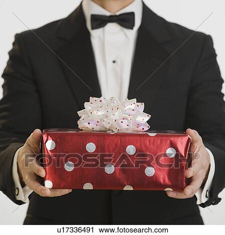 Stock Image - Man in tuxedo holding gift. Fotosearch