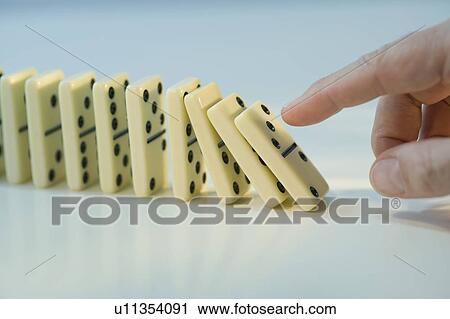 Stock Image - Man pushing row of dominoes. Fotosearch