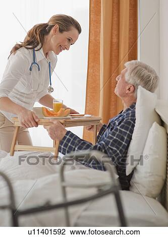 Stock Image - Nurse giving senior man breakfast. Fotosearch