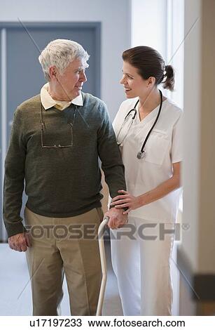 Stock Image - Nurse helping senior man with cane. Fotosearch