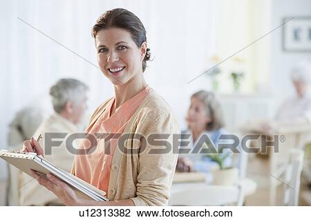 Stock Image - Nurse writing on patient’s medical chart. Fotosearch