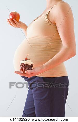 Stock Image - Pregnant woman holding healthy and unhealthy snacks. Fotosearch
