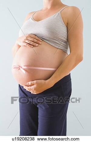 Stock Photo - Pregnant woman’s belly wrapped in pink ribbon. Fotosearch