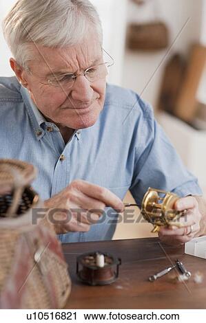 Stock Image - Senior man fixing fishing reel. Fotosearch