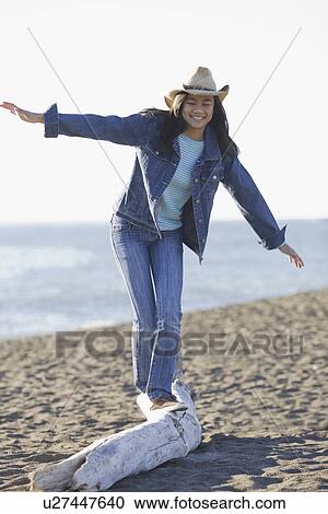 Stock Image - Teenage girl balancing on driftwood. Fotosearch